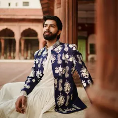 Here, tradition meets a modern aesthetic. A crisp white pleated kurta is layered with a navy blue Nehru jacket, featuring stunning silver floral embroidery that feels both classic and contemporary, perfect for a man with discerning taste.