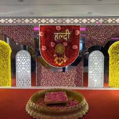 For a grand haldi ceremony, this stage features a backdrop of red and yellow flowers with elegant white arches. The lotus-shaped seating area is filled with fresh flower petals.