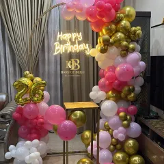 Pretty in pink and gold for a stylish 26th birthday. This setup includes a half-arch of balloons, a custom neon sign, and a golden pedestal for the cake, creating a chic and celebratory corner perfect for photos.