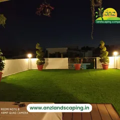 A simple yet elegant terrace setup featuring high-quality artificial grass. The space is illuminated by globe lights and accented with spiral topiaries, creating a clean and peaceful ambiance at night.