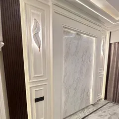 This image shows a luxurious wall panel design combining dark wood, white molding, and a marble-finish insert. The feather-shaped wall lights add an artistic and delicate touch.