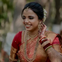 A close-up of this beautiful bride's happy expression. Her makeup features defined eyes and a warm lip color, perfect for her red and gold silk saree.