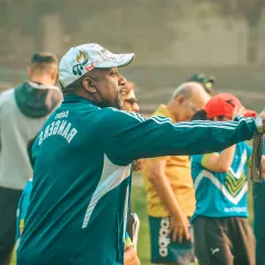 A senior coach directs his players from the sideline, his experience guiding the team's performance.