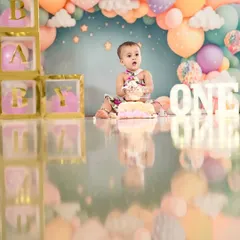 A sweet first birthday cake smash. This little girl is surrounded by a beautiful pastel balloon arch, creating a dreamy and festive scene.