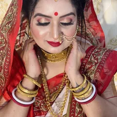 This is a classic Bengali bridal look, identifiable by the white and red saree, the large red bindi, and the traditional gold jewellery. I create authentic looks for all traditions.