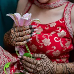 A close-up shot of the bride's hands holding a lily, showcasing the beautiful jaali (net) pattern on her mehendi.