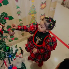A close-up of a little girl in a festive plaid dress carefully placing an ornament on the tree. These moments of focused participation are what make the holidays special.