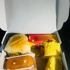 A simple yet satisfying snack box option featuring a classic vada pav, soft dhokla, a sweet cake, and a juice box. These are ideal for quick distribution at events or as a travel snack.