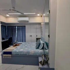 A full view of a master bedroom with a cool blue color scheme, floor-to-ceiling wardrobes, and an integrated study or dressing table. The mirrored wardrobe panels make the room feel larger.
