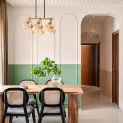 This dining corner features a two-tone wall with sage green paint and arched beadings, creating a sophisticated backdrop. The wooden table, wicker-back chairs, and a statement chandelier complete this elegant and modern dining space.
