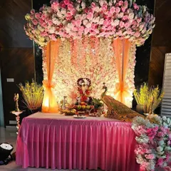 For a truly royal feel, I created this stunning Ganpati mandap with a ceiling completely covered in pink and white flowers. The backdrop is a wall of white flowers, with peach drapes and a beautiful peacock figurine adding to the grandeur.