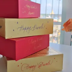 A stack of festive gift boxes personalized for Diwali. The combination of red and gold boxes with calligraphy in different colors creates a vibrant and joyful presentation for holiday gifting.