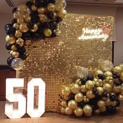 Celebrating a golden anniversary with a spectacular gold sequin backdrop. This decoration for a 50th anniversary features marquee numbers, a "Happy Anniversary" neon sign, and a lush garland of black and gold balloons.