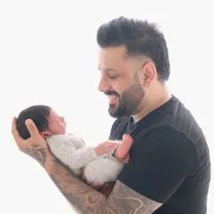 A proud father with tattooed arms smiles as he holds his tiny newborn, showcasing a beautiful contrast between strength and gentleness.