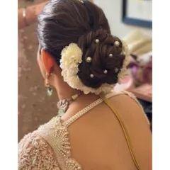 A close-up of a textured bridal bun. The combination of white flowers and scattered pearls creates a look of pure elegance, perfect for a pastel lehenga.