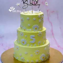 A magnificent three-tier daisy-themed cake for a 5th birthday. The bright yellow cake is covered in beautiful, handcrafted fondant daisies for a cheerful and impressive look.