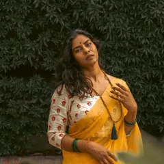 A powerful close-up portrait taken outdoors against a lush green backdrop. I focus on capturing authentic expressions and the intricate details of traditional wear, like this beautiful saree and printed blouse.