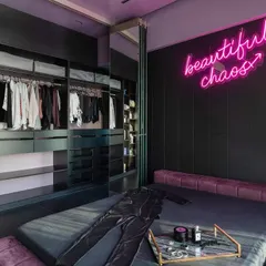 This open-concept wardrobe uses glass doors to create a boutique-like display for clothes and accessories. The dark, moody color scheme paired with the neon sign gives the room a bold, personal feel, proving that a wardrobe can be a central design feature of a bedroom.