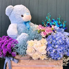 A sweet and cuddly gift perfect for a new baby or just to send some love. This wooden crate is filled with a soft blue teddy bear nestled among blue hydrangeas, carnations, and other fresh seasonal blooms.
