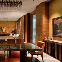 The dining area of a Gurgaon home, where rich textures of wood and stone create a warm and inviting atmosphere. A modern chandelier adds a touch of glamour, while the large windows keep the space connected to the outdoors.