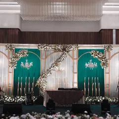 An engagement and Sangeet stage that blends classic romance with modern flair. The design uses an emerald green and white palette, with floral arches, chandeliers, and elegant candle stands.
