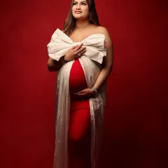 A stunning frontal view of the mother-to-be, wrapped like a precious gift in a red gown and a large white bow. This portrait is a beautiful way to celebrate a pregnancy during the festive season.