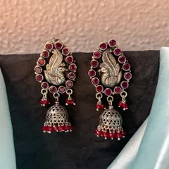 Beautiful pure silver jhumkas. This pair features a peacock motif surrounded by ruby-red stones, with a classic jhumka bell drop adorned with matching red beads.