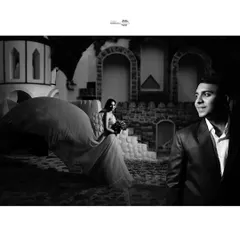 A cinematic black and white shot where the bride's flowing gown takes center stage. The groom looks on, creating a narrative of admiration and romance.