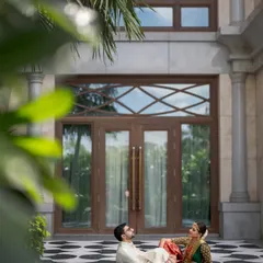 A quiet moment for the couple amidst the wedding festivities. This wide shot showcases their beautiful traditional outfits against the stunning architecture of the venue, the Leela Palace in Chennai.