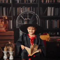 A young wizard smiles as he reads a book of spells. This photo highlights the warm, enchanting atmosphere we create with careful lighting and detailed props for our Harry Potter sessions.