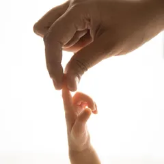 The delicate touch between a parent's hand and their baby's tiny fingers. This backlit, artistic shot highlights the beautiful, fleeting details of the newborn stage.