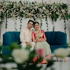 The couple seated against a stunning backdrop of white and blush flowers. The rich teal sofa provides a beautiful pop of color, making this a perfect photo corner at their engagement party.