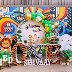 We created this vibrant jungle theme for Shivaay's "Wild One" birthday party. The setup features cute cartoon animal cutouts, animal print "ONE" letters, and a green and gold balloon arch against a unique graffiti wall.