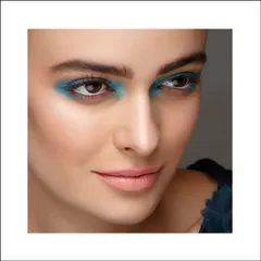 An editorial beauty shot with a pop of bright blue eyeshadow. The focus is tight on the eyes, showcasing a bold makeup choice with clean, luminous skin.
