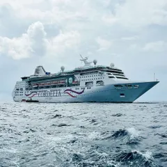A dramatic shot of the Cordelia cruise ship on the open sea. The perspective emphasizes the vessel's size and the vastness of the ocean, creating a sense of adventure and escape.