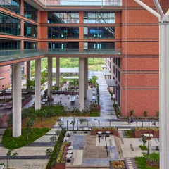 The Wipro Hyderabad Campus features a central plaza that acts as the heart of the community. This multi-level space, with its blend of hardscape and softscape, provides various zones for interaction, from casual seating areas to open pathways, all sheltered and cooled by the surrounding architecture.