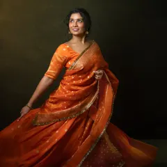 Movement and color come together to tell a story of joy and transformation. Vennela, in a vibrant orange saree, embodies the confidence she has cultivated over her journey from a shy child to a global entrepreneur. This shot captures the pure, uninhibited energy of a woman who has found her voice.