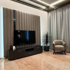 A closer look at the TV unit in the master bedroom. The wall features soft, vertical upholstered panels and a central mirror, creating a sophisticated backdrop. The dark, curved console adds a touch of modern elegance.