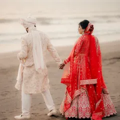 A walk to remember along the beach. This shot captures the couple hand in hand after their ceremony, with the bride's red lehenga vibrant against the sand.