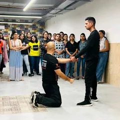 I demonstrate a technique from a kneeling position to show that defense is possible from any angle or situation. The audience of female professionals watches intently, learning how to adapt to unexpected scenarios.