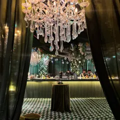 A dramatic entrance to the enchanted forest bar area. A large crystal chandelier hangs between deep green curtains, inviting guests into a space of elegance and mystery.