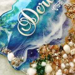 A close-up of the ocean nameplate, showing the detailed texture of the sand, shells, and the lacing of the waves.