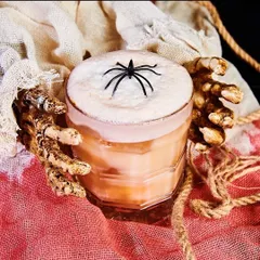 Don't get caught in this web! A creamy, spooky cocktail garnished with a black spider, held by skeleton hands. Perfect for your next Halloween party.