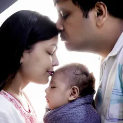 A classic and emotional family pose. The parents gently kiss their newborn's forehead, creating a beautiful silhouette filled with love and tenderness.