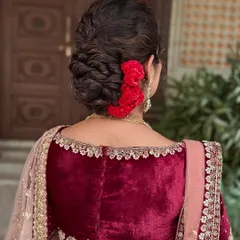A modern yet royal messy classic updo. This hairstyle, decorated with fresh red flowers, is the perfect complement to a glamorous Sangeet or Reception lehenga.