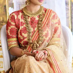 This sublime bridal lehenga features a cream-colored base with intricate red and gold threadwork on the blouse. The sheer net dupatta with a striped border adds a layer of delicate elegance to the entire outfit.