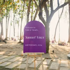 The entrance to "Sunset Vows." A simple, elegant sign in a bold purple hue sets the tone for a modern, stylish beach wedding, guiding guests toward the magic about to unfold.