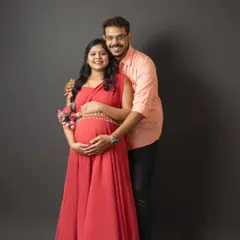A beautiful couple's maternity portrait. The expecting mother in her red gown is complemented by fresh flowers, adding a touch of natural elegance to the shot.