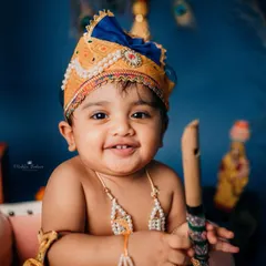A happy 'Kanha' holding his flute and smiling directly at the camera. The joy in his eyes makes this a truly special portrait from his Janmashtami baby photoshoot.
