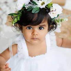 A stunning close-up of the baby girl with a floral crown, her big, expressive eyes looking directly at the camera.